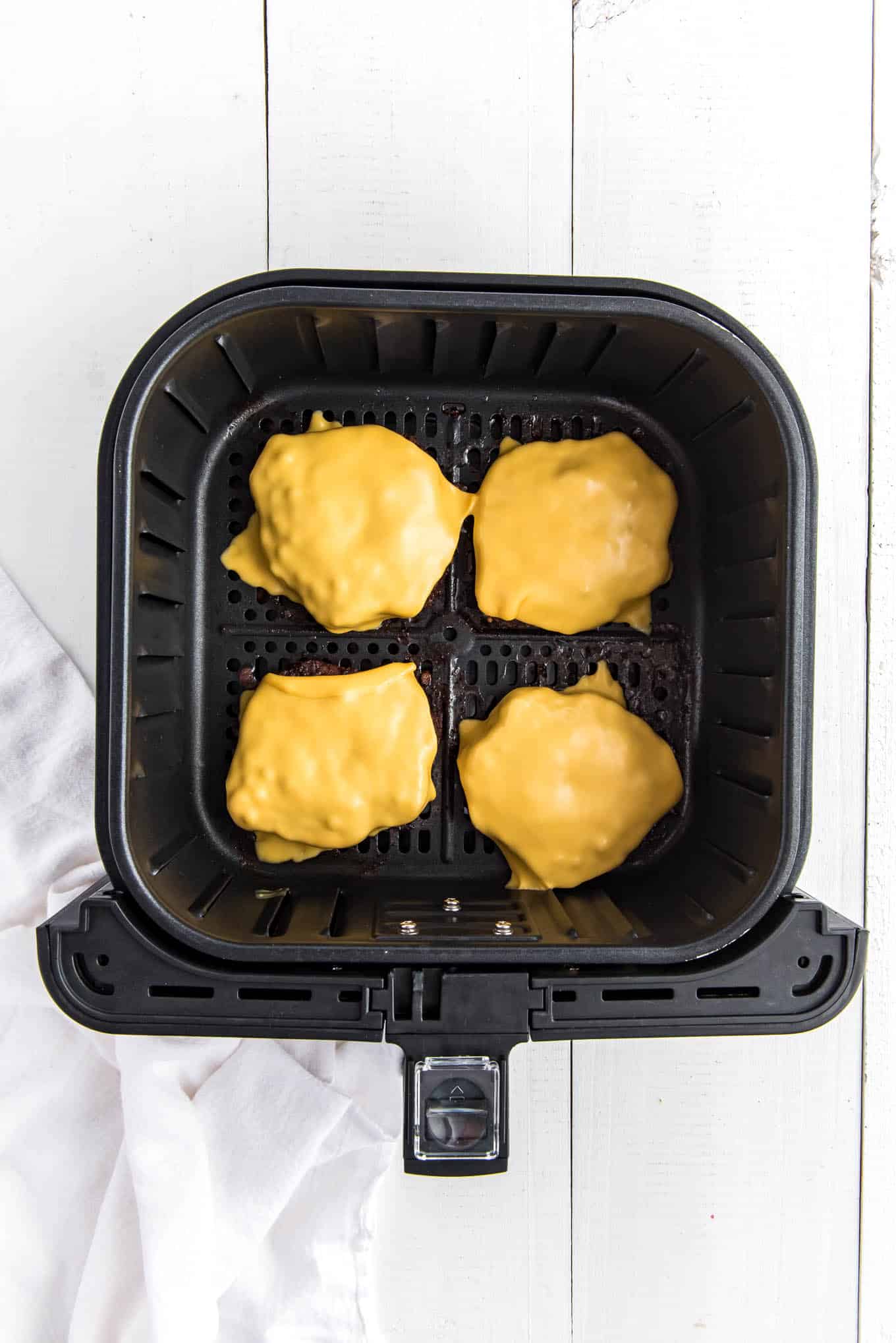 Frozen burgers in the air fryer are topped with melted cheese.
