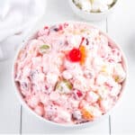 A white bowl on the table filled with fruit salad with Cool Whip.