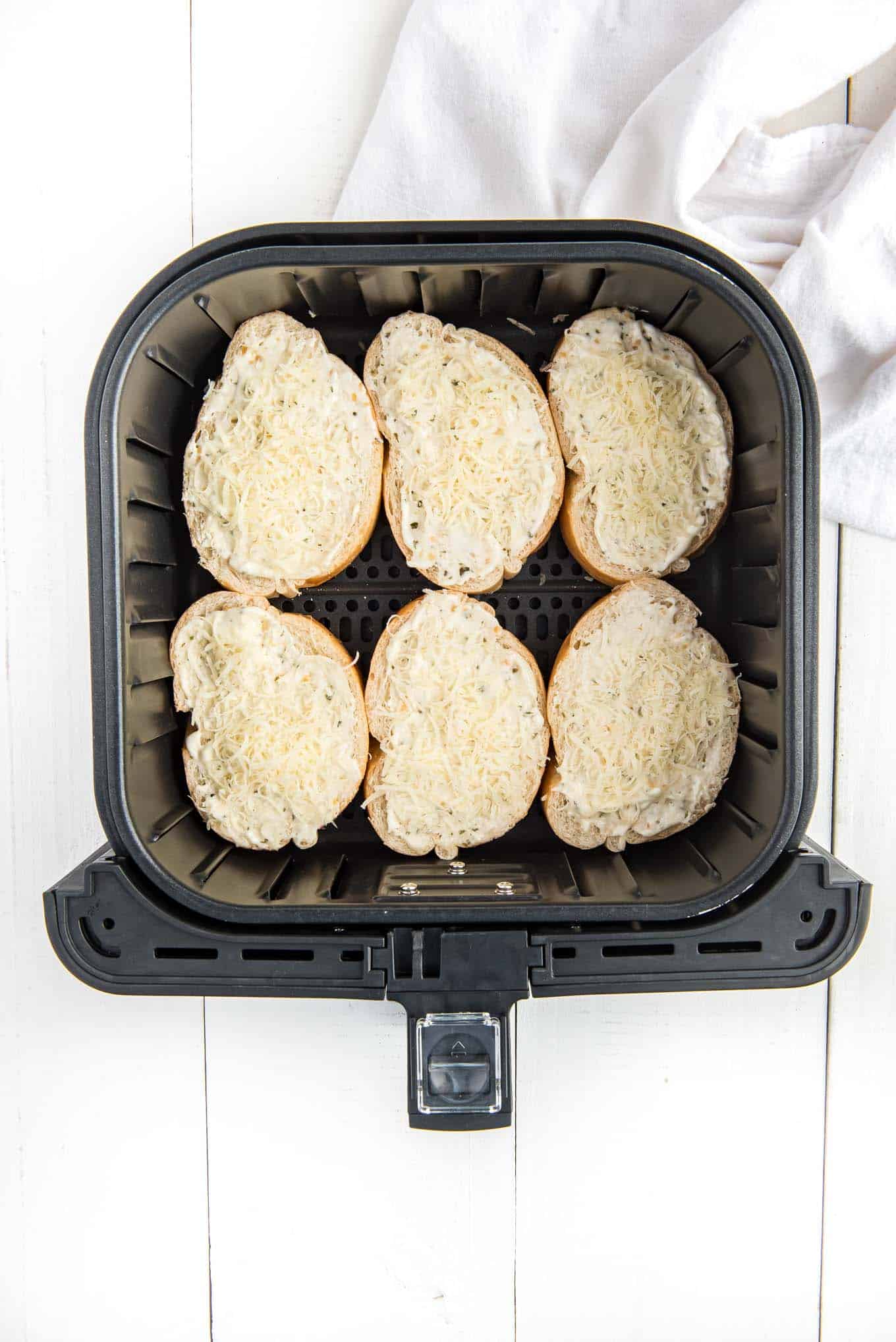 Pieces of french bread topped with butter and parmesan cheese in an air fryer basket.