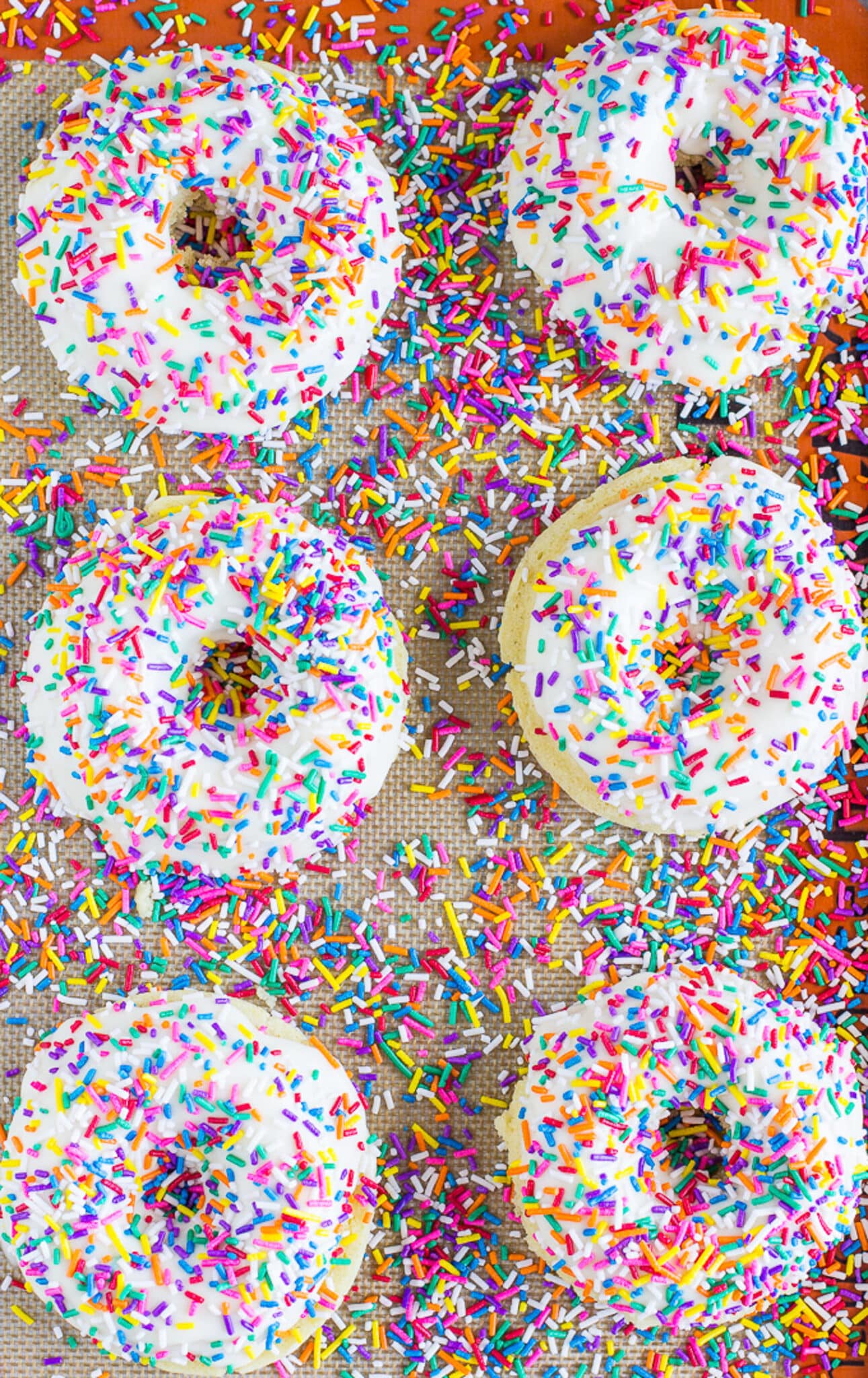 Overhead of baked donuts on a silpat topped with vanilla glaze and sprinkles.