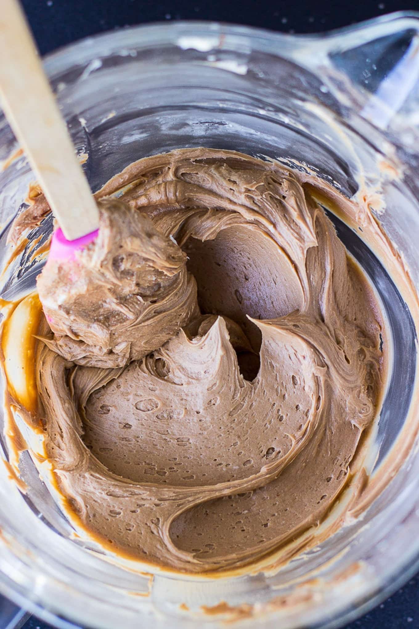 Chocolate frosting in a glass bowl with a spatula stirring it around.