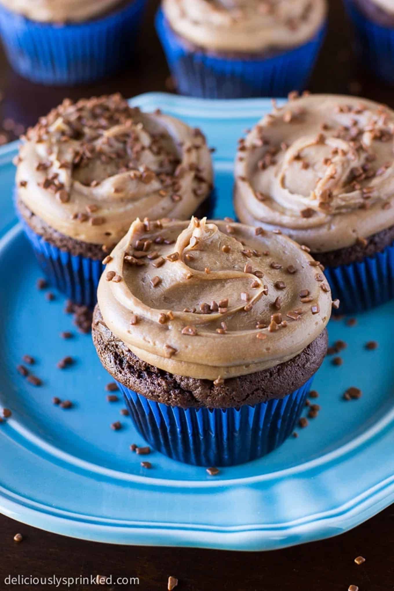 Cupcakes on a plate with chocolate buttercream frosting and bits of chocolate sprinkles on top.