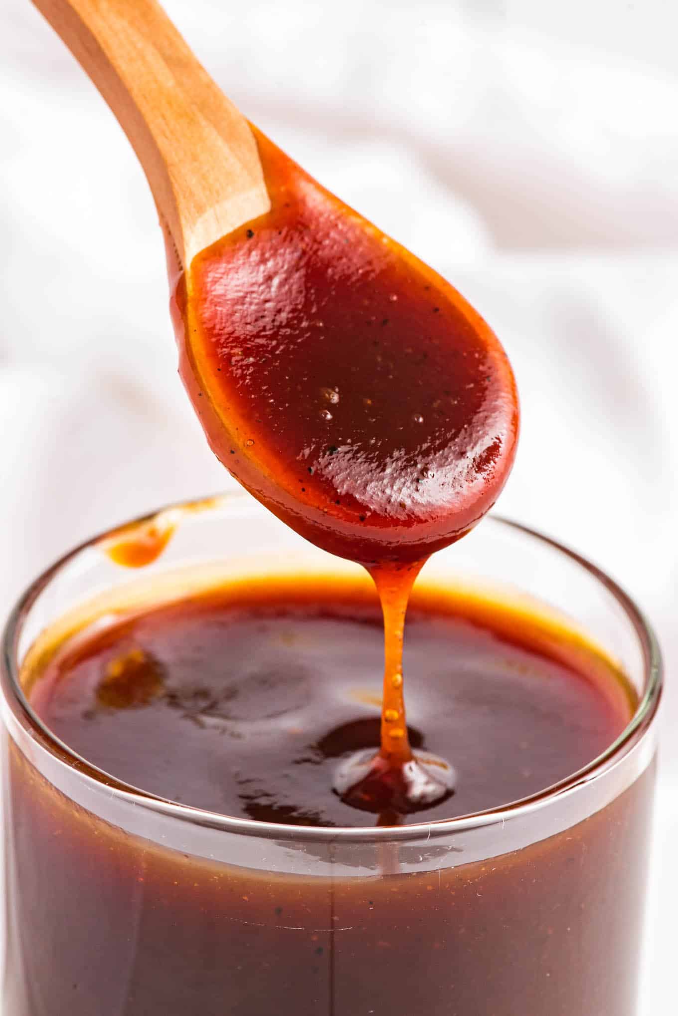 A spoonful of BBQ sauce dripping back into the jar of sauce.