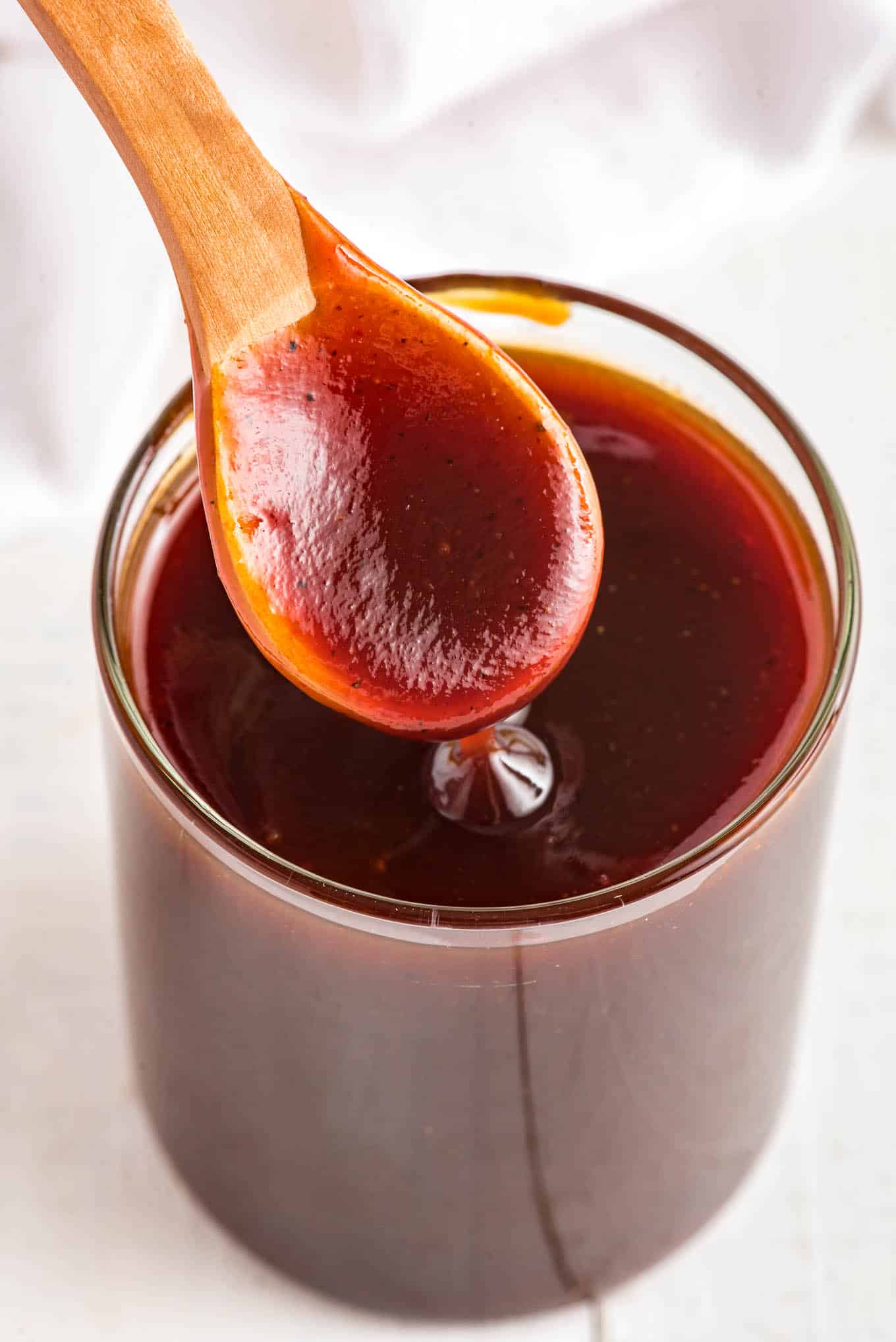 A spoon up over the jar of BBQ sauce with a bit of the sauce in it.