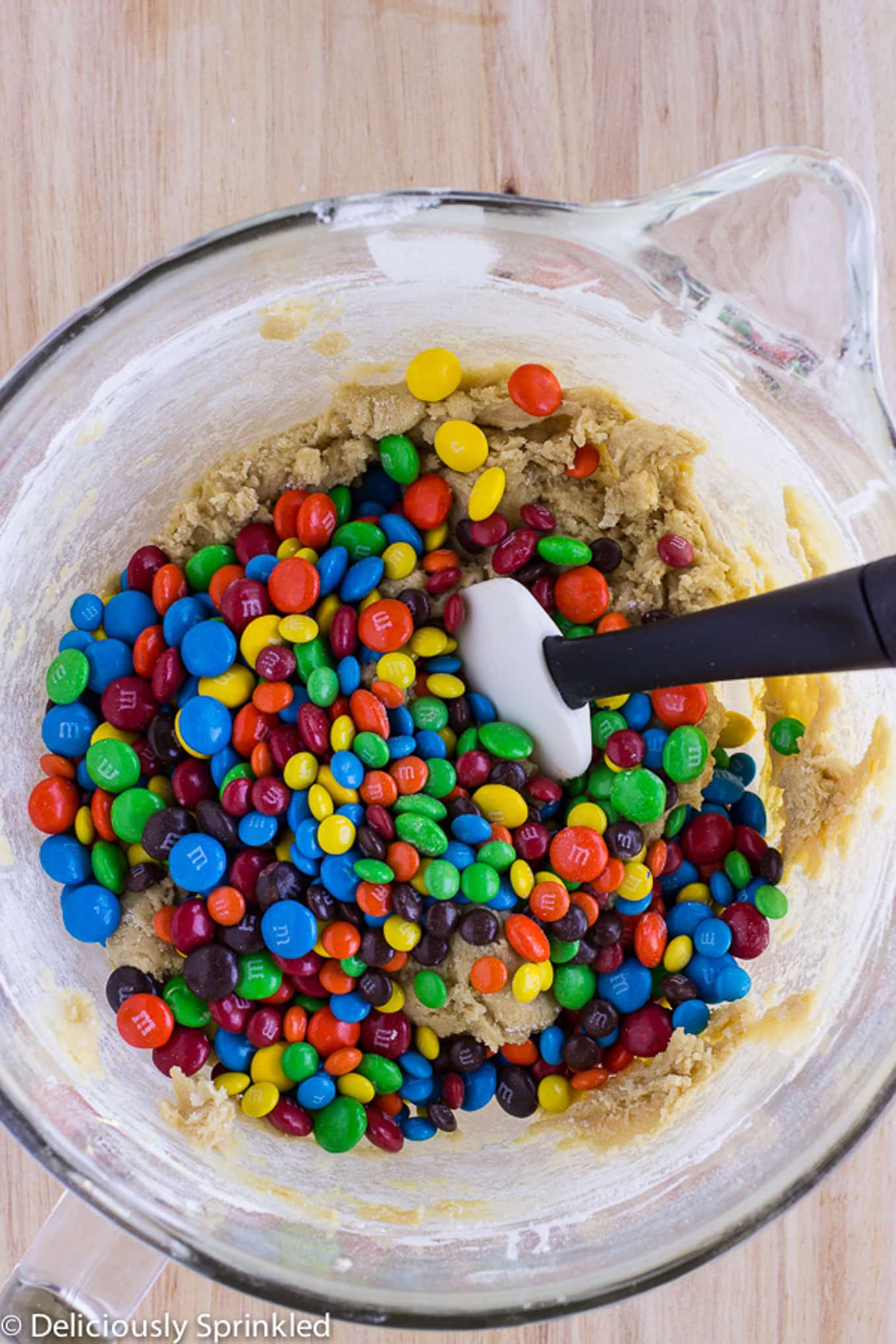 M&M cookie dough in a mixing bowl with a spatula.