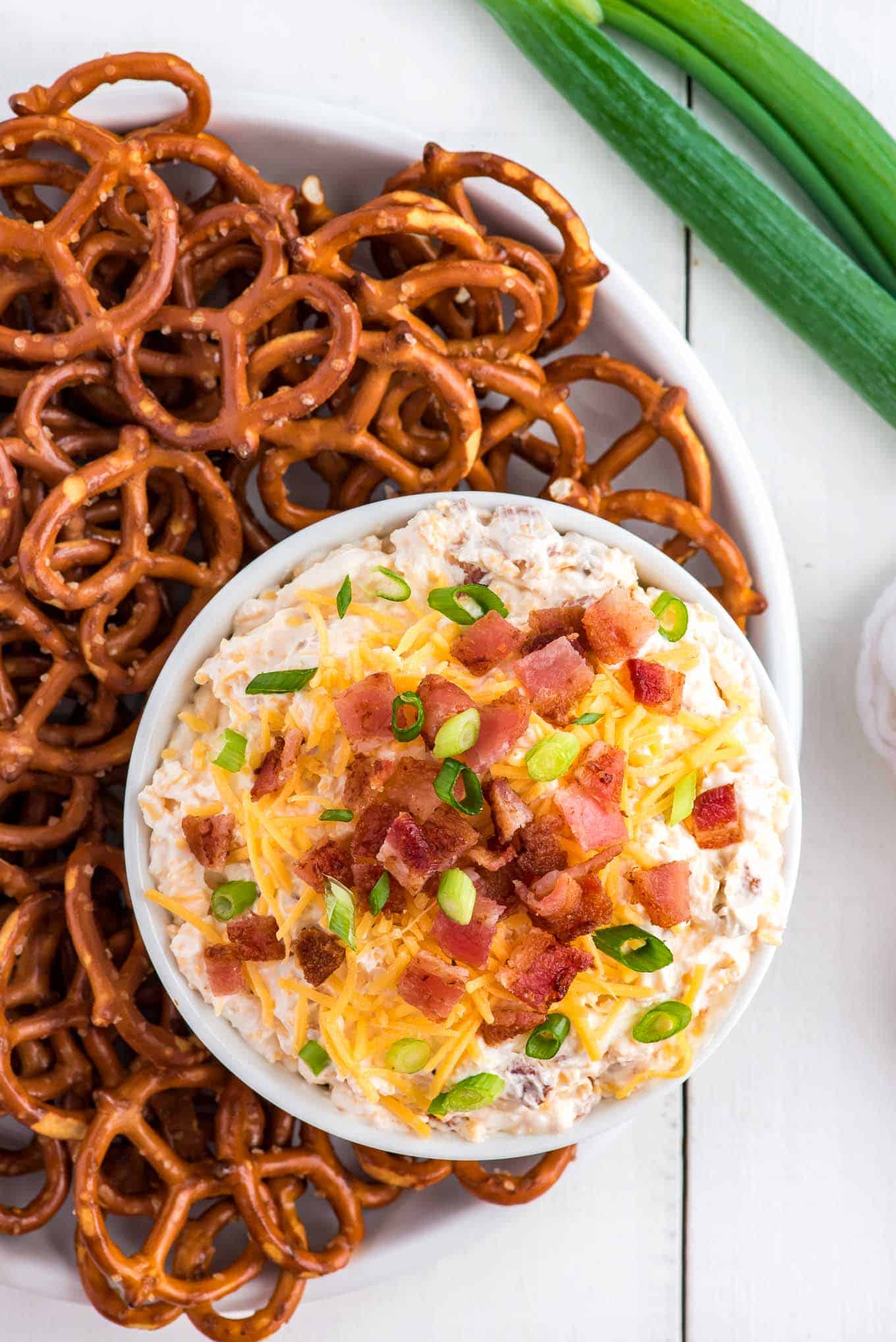 A bowl of pretzel dip on a platter with pretzels for dipping around it.