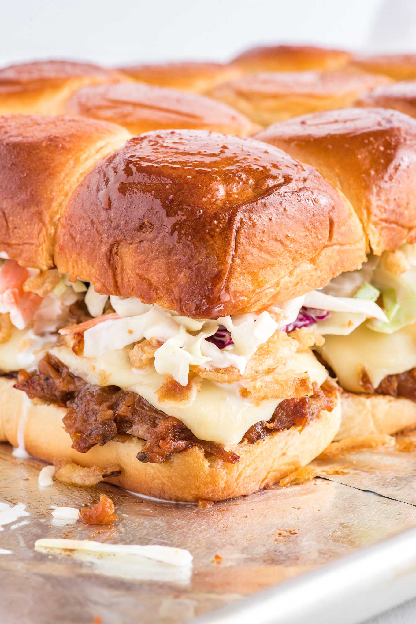 Pulled pork sliders on a baking tray with layers of pork, cheese, onions, and slaw.