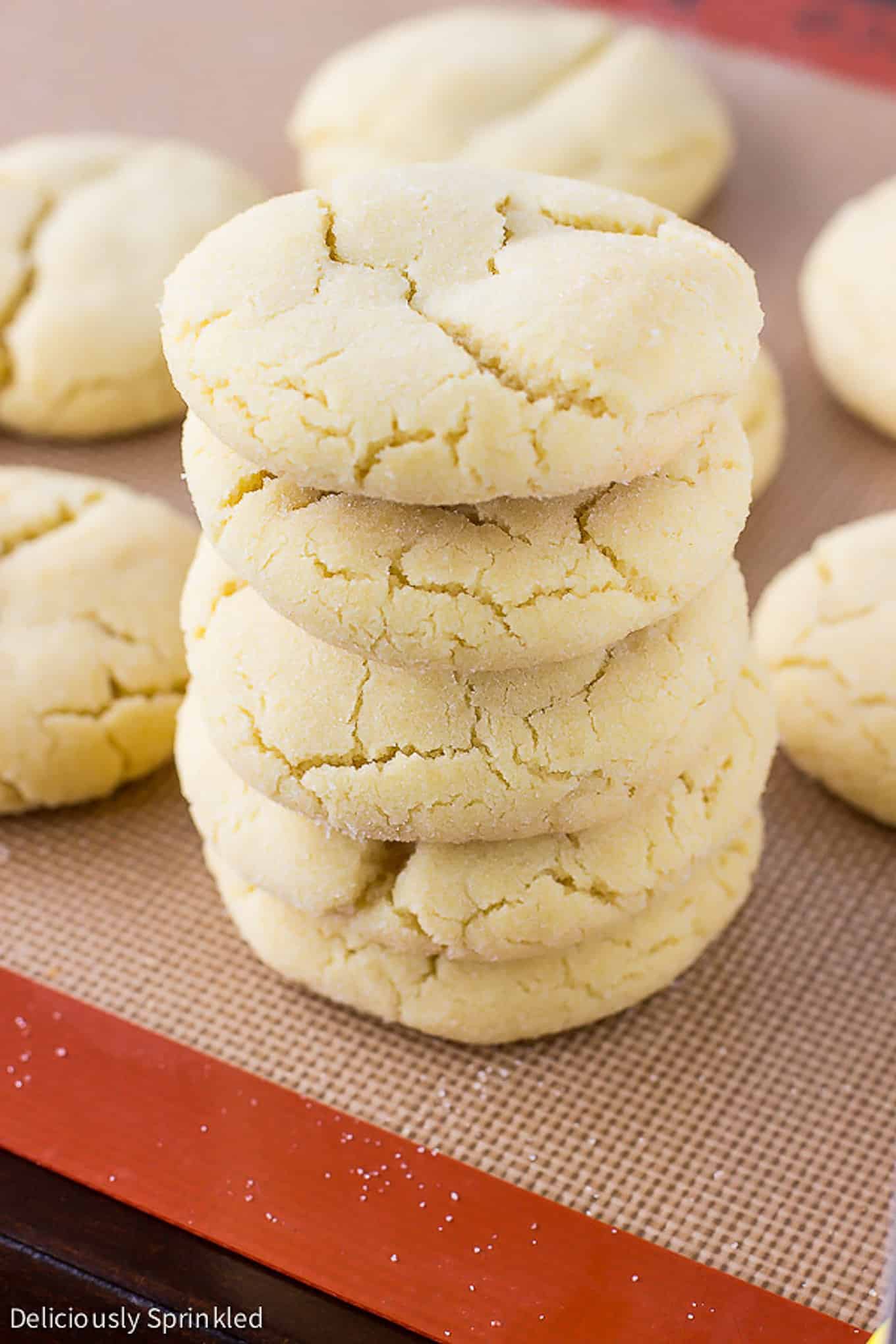 A stack of five sugar cookies on the front corner of a baking tray with more cookies in the background.