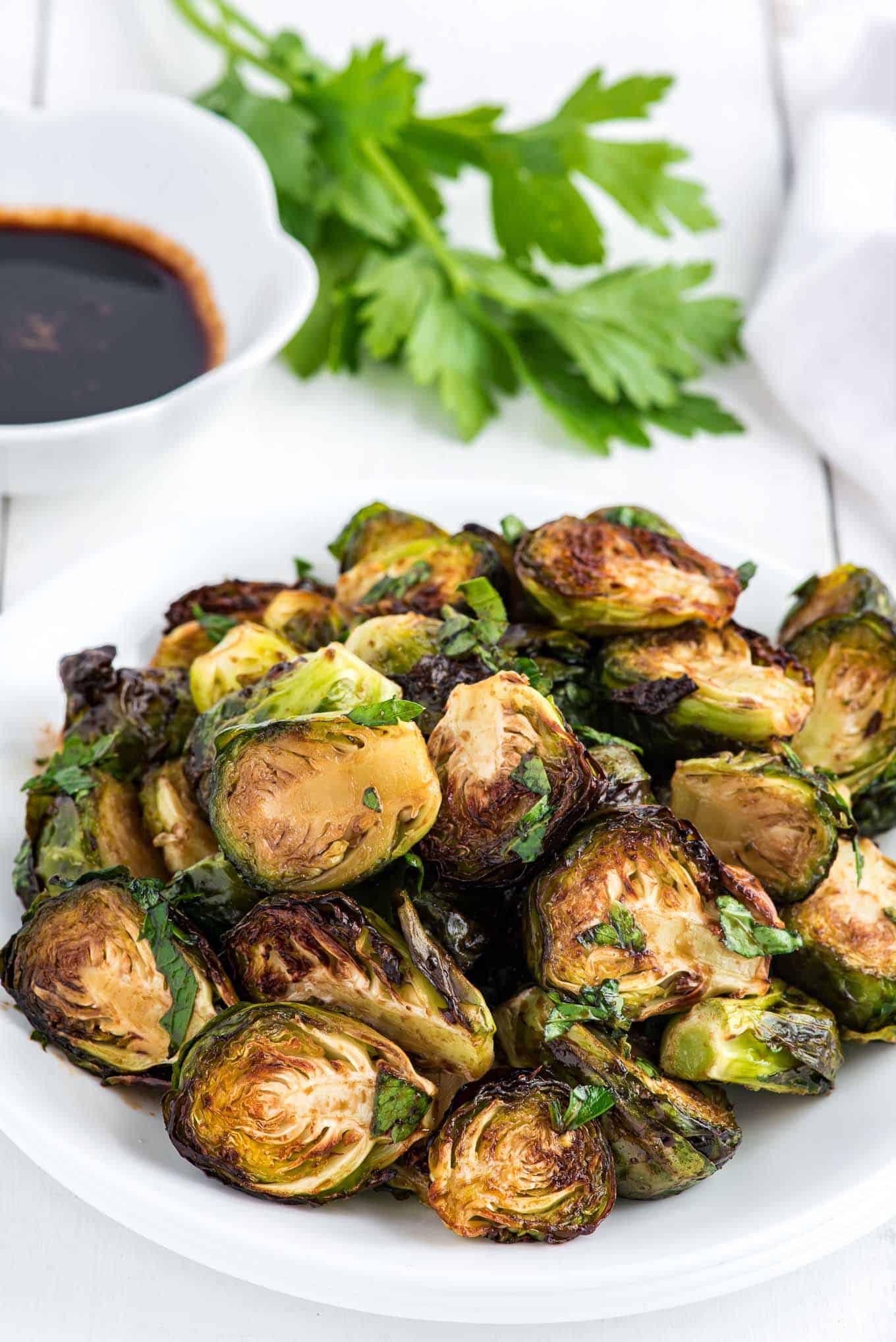 A plate of air fryer Brussels sprouts on the table with a bowl of balsamic glaze in the background.