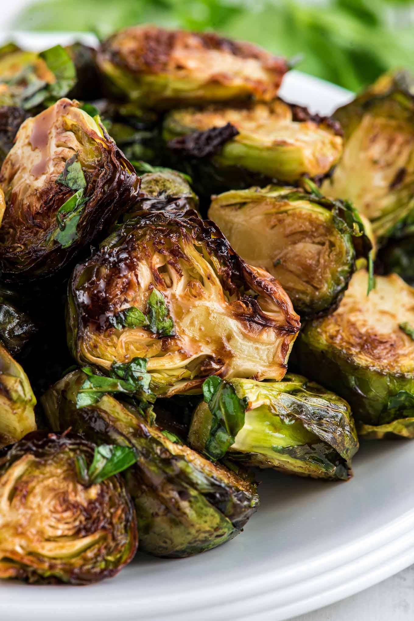 A close up of Brussels sprouts cooked in the air fryer served up on a white serving bowl. 