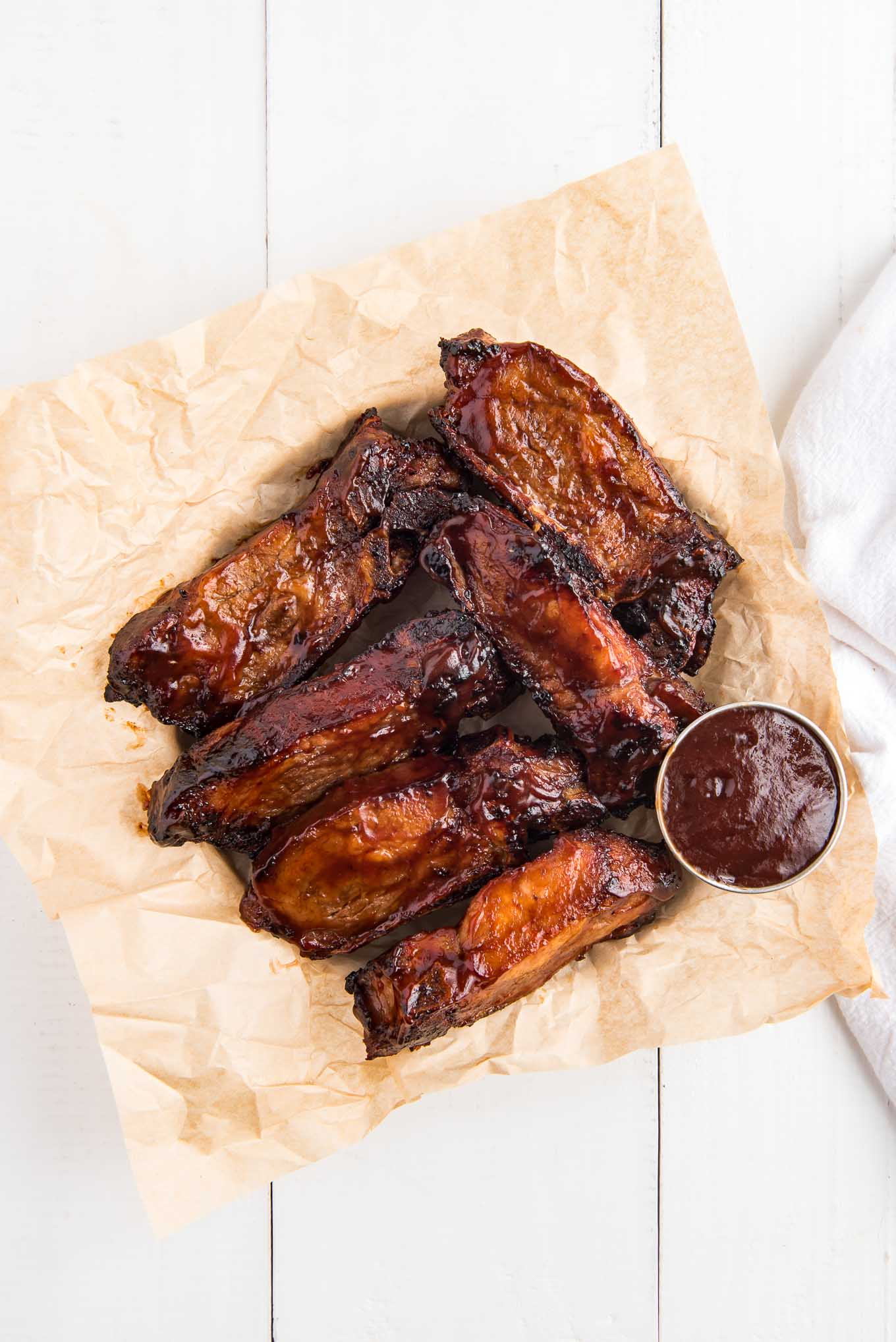 BBQ country style ribs in the air fryer served up in a bowl lined with parchment paper and a little ramekin of sauce.