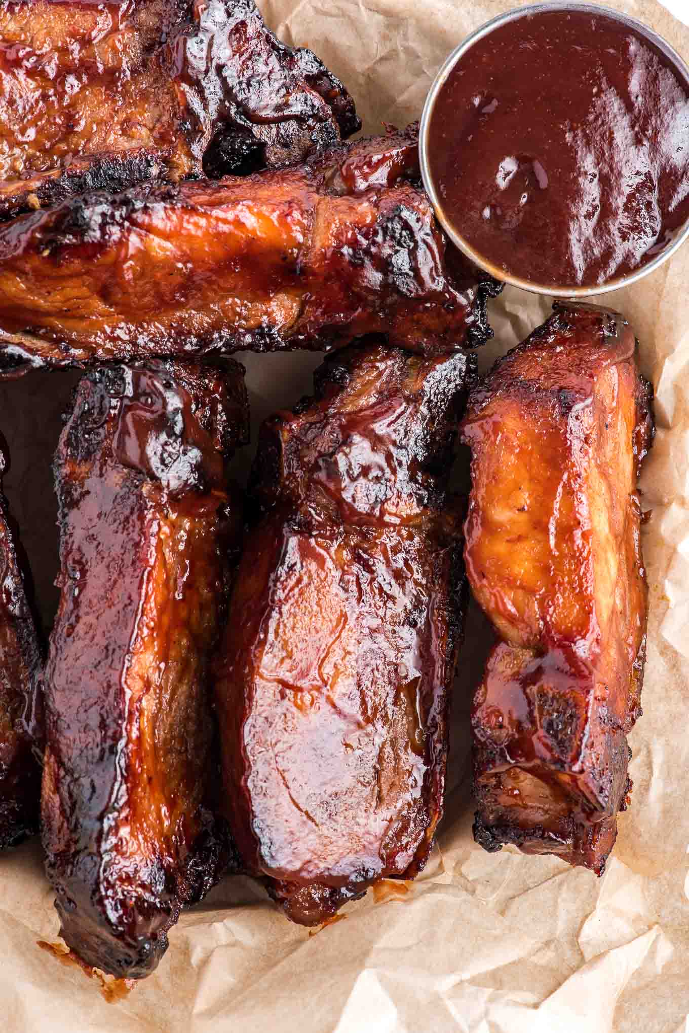 Air fryer country style ribs on brown parchment paper with a ramekin of BBQ sauce to the side.