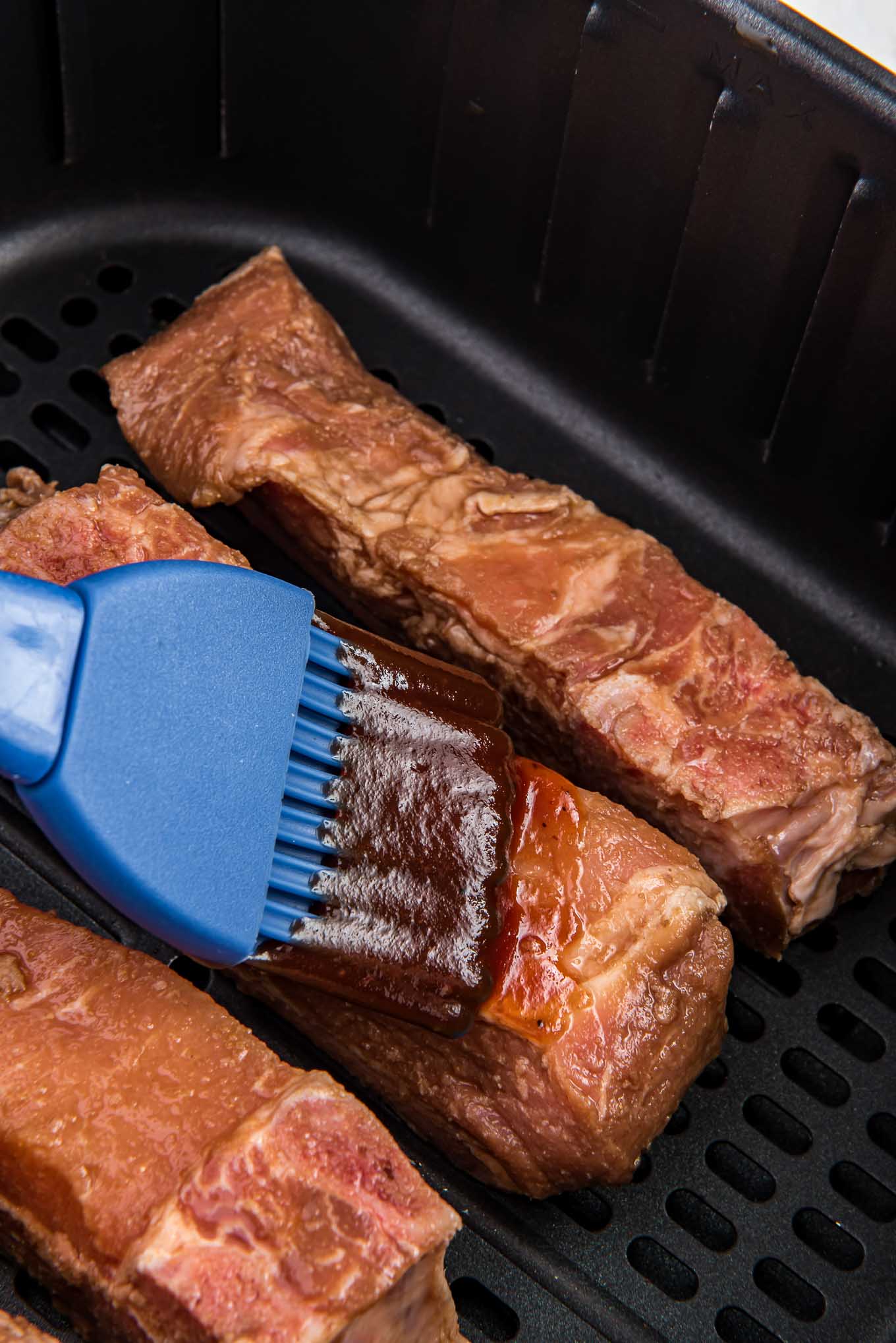 Brushing the country style ribs with BBQ sauce in the air fryer basket.