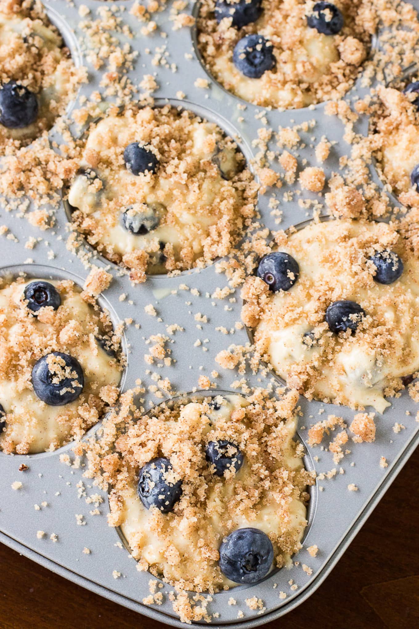 Blueberry muffin batter in a baking pan with blueberries on top and a crumb topping.