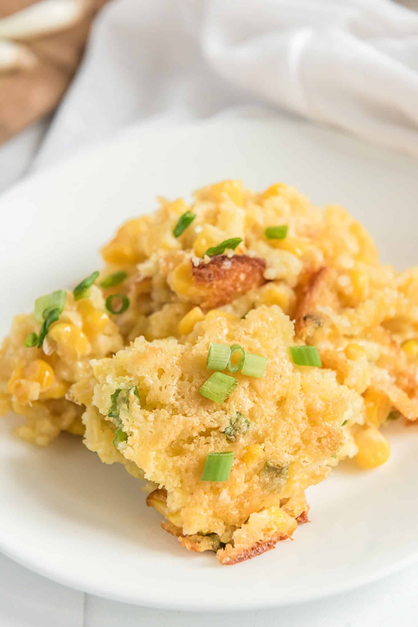 A serving of corn casserole served up on a white plate with green onions on top.