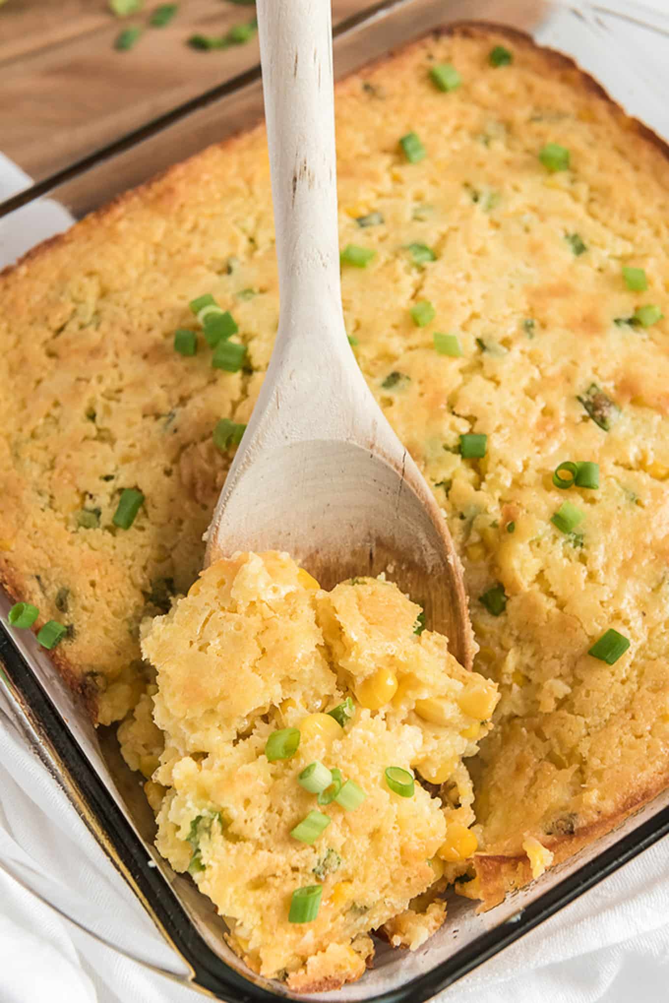 A spoon lifting a serving of Jiffy corn casserole up from the baking dish.
