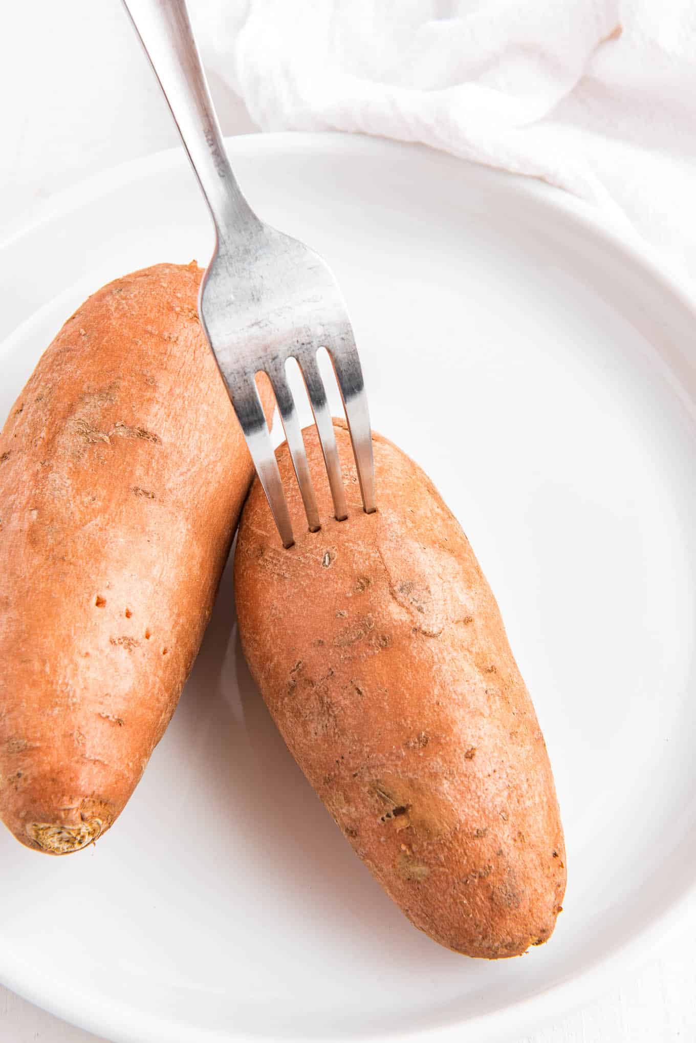 A fork piercing holes in the sweet potatoes on a plate.