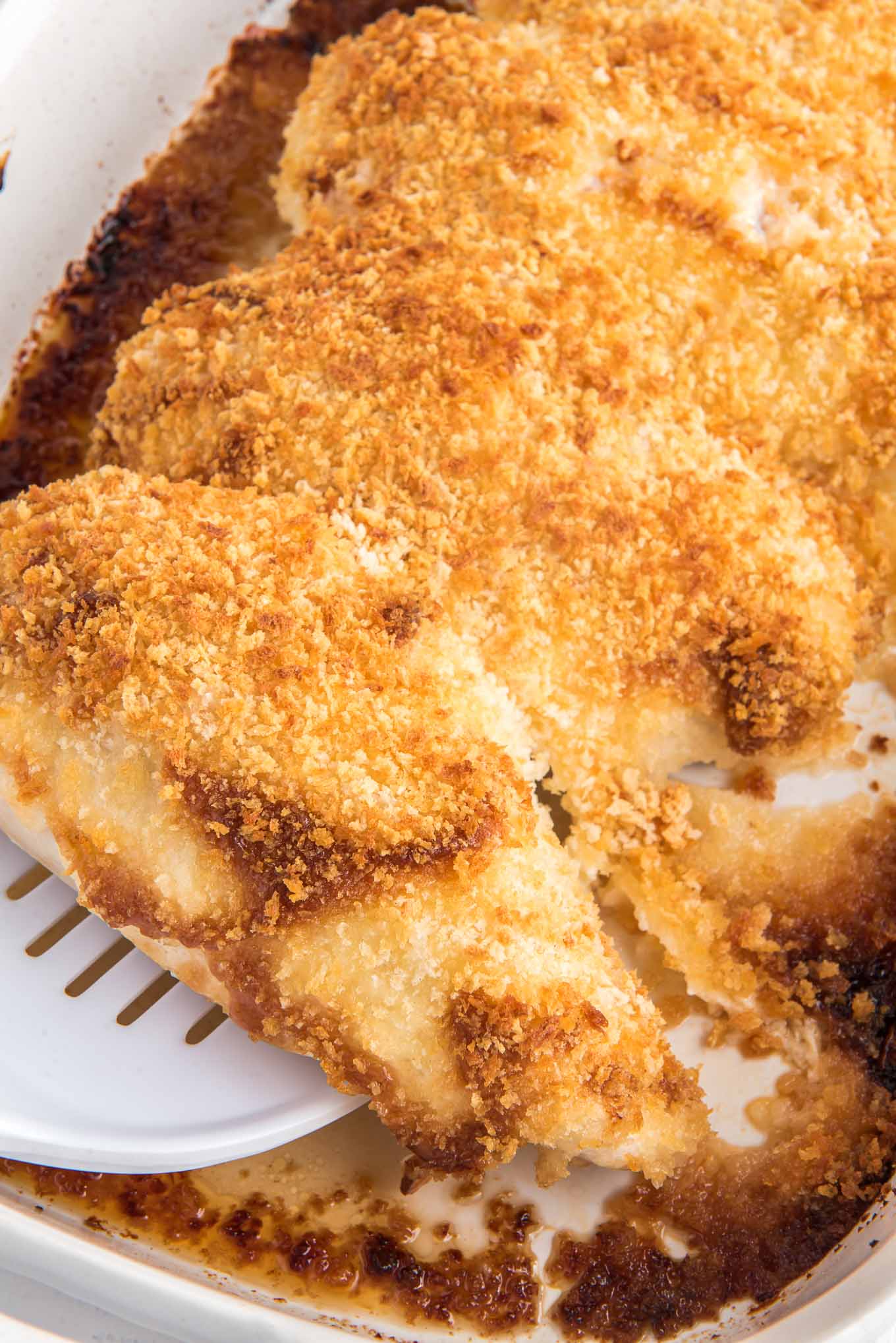 Crispy panko chicken breasts in a baking dish with a spatula lifting one up to serve.