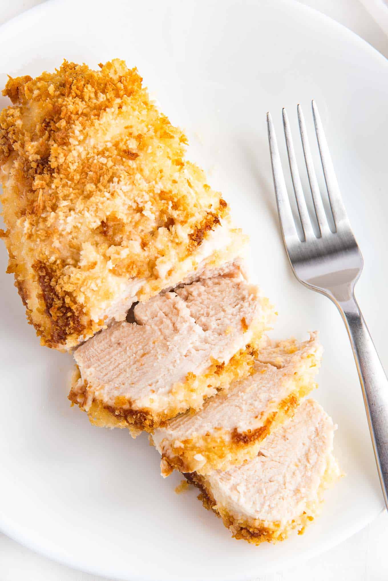  A piece of crispy panko chicken on a plate with a fork to the side.