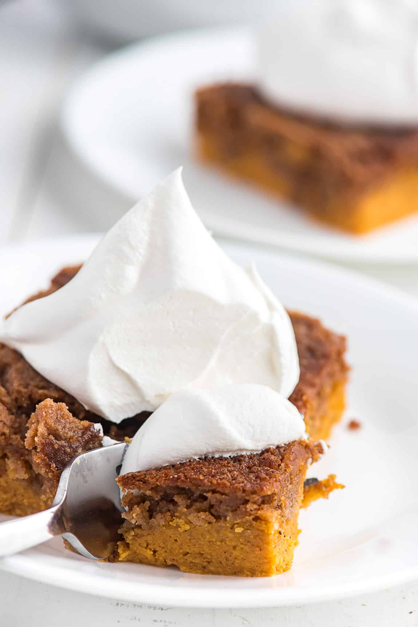 Pumpkin cake on a plate topped with cool whip with a fork on the side. 