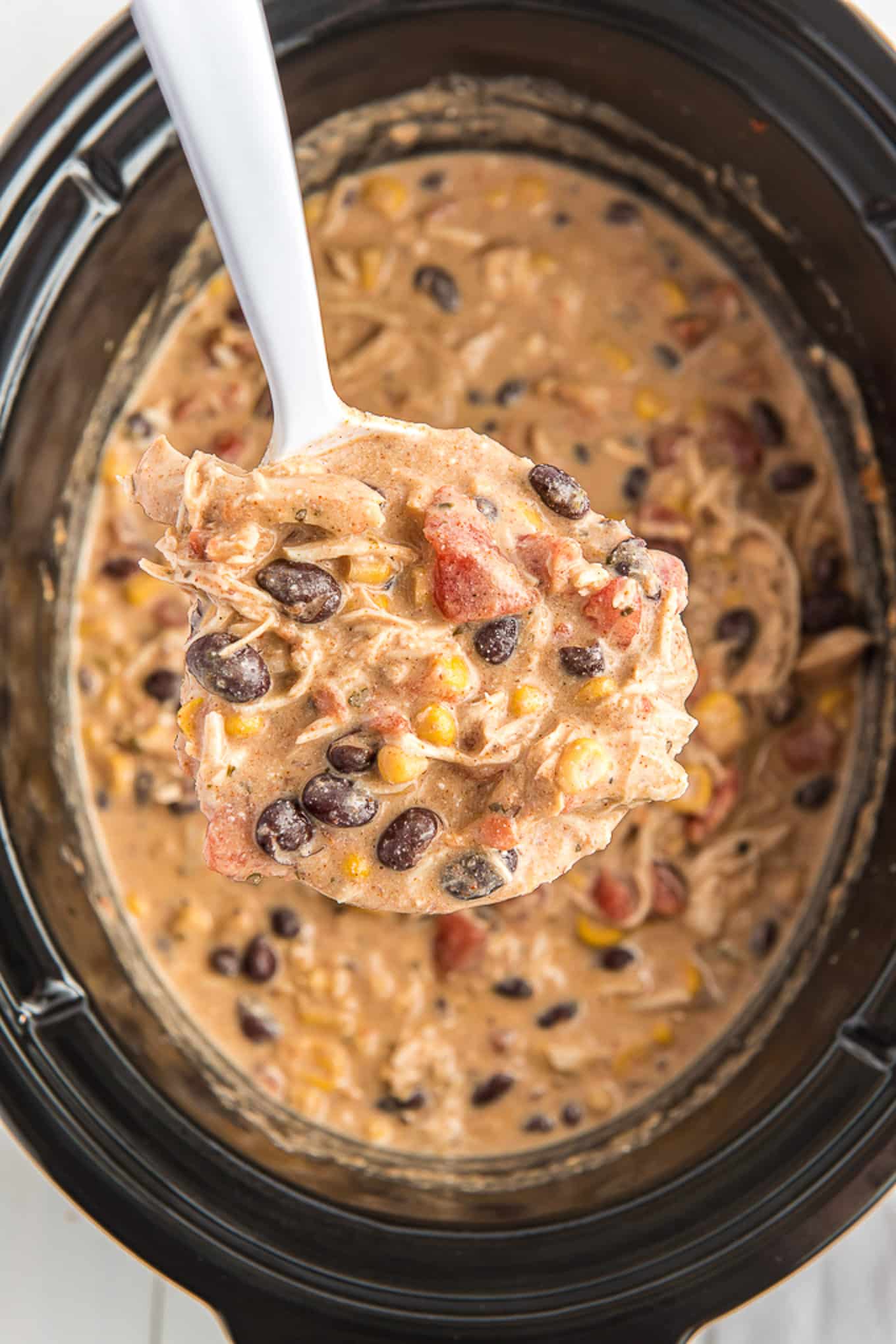 Crockpot white chicken chili in the slow cooker with a ladle lifting up a spoonful.
