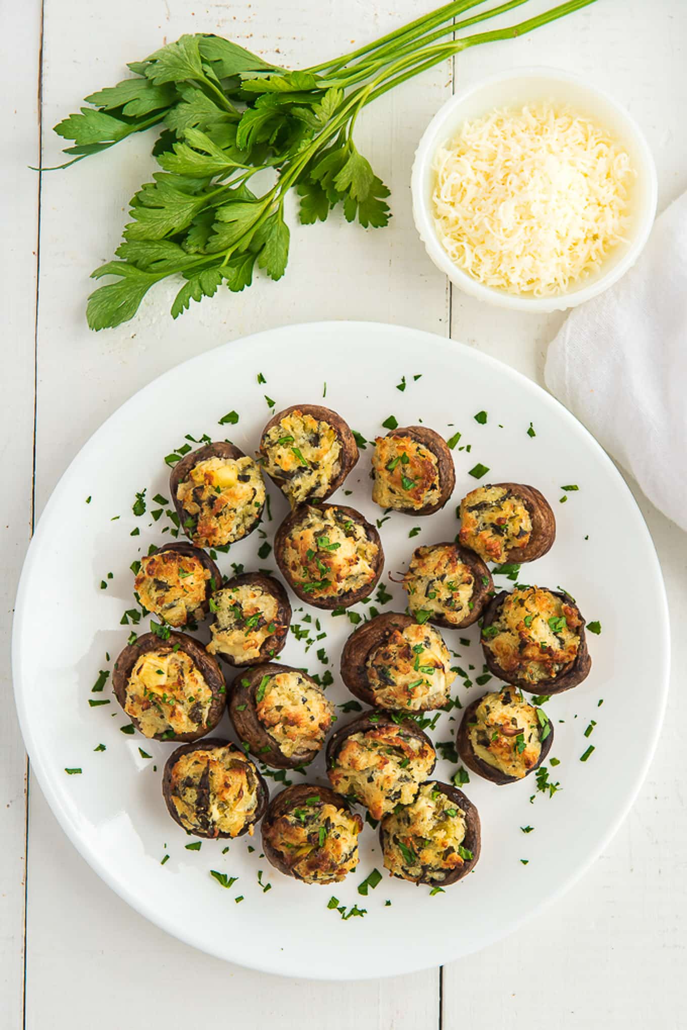 Air fryer stuffed mushrooms on a white plate with a bowl of parmesan cheese and parsley to the side.