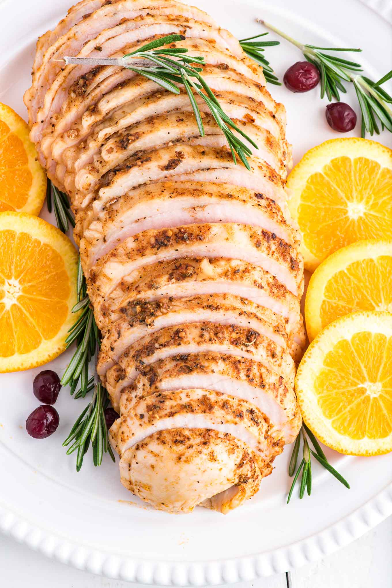 Oven roasted turkey breast sliced on a platter and surrounded by rosemary, citrus, and cranberries.