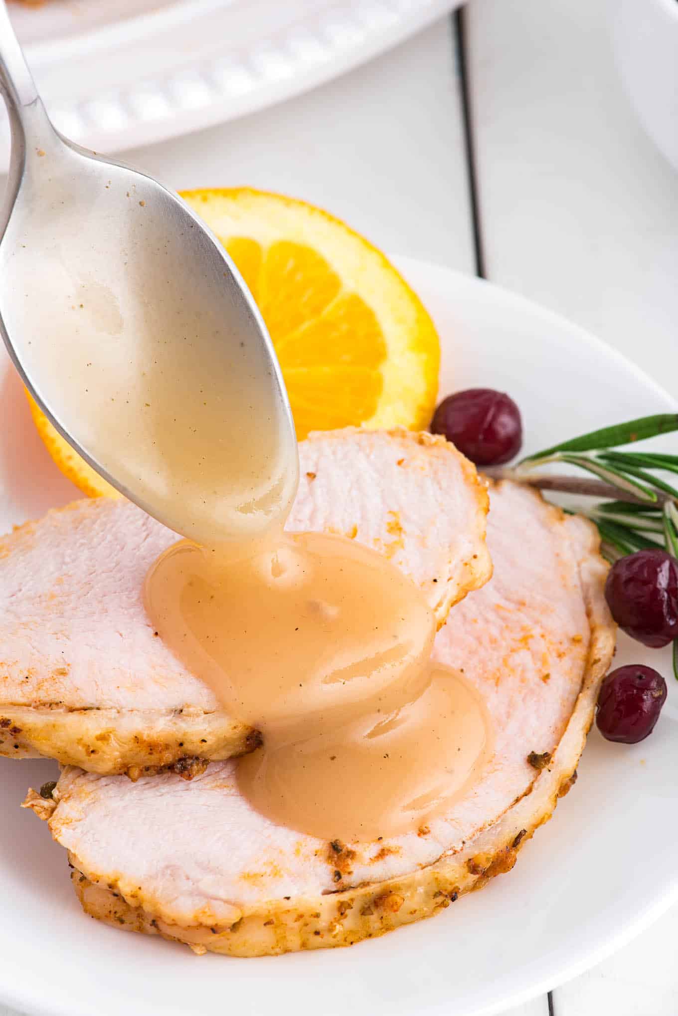 Spooning turkey gravy over two slices of roasted turkey breast sliced on a plate.