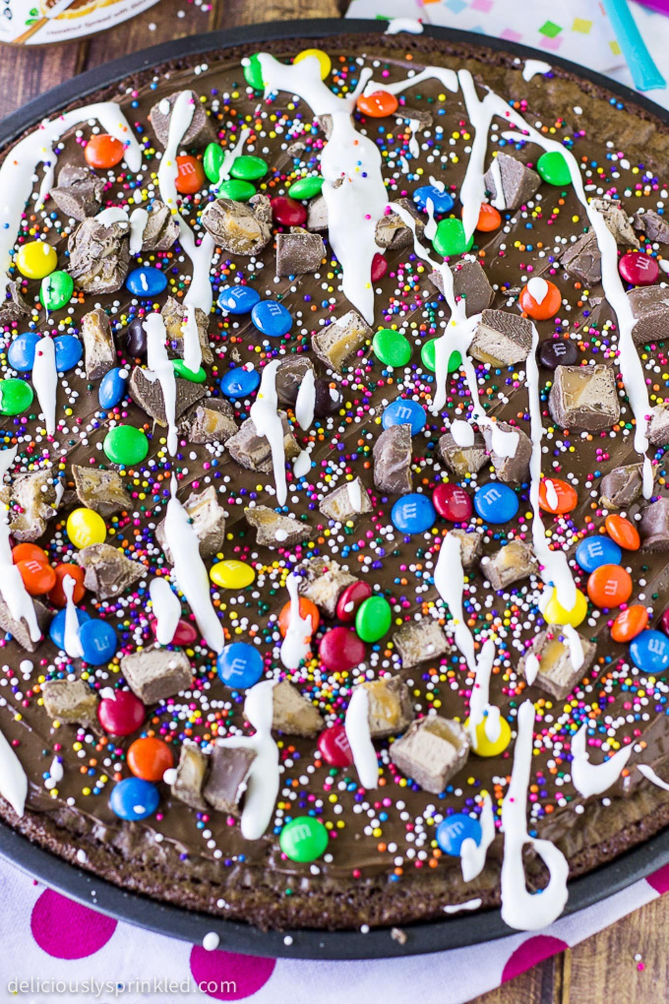 Brownie dessert pizza in a pan topped with marshmallow cream, candy, and sprinkles.