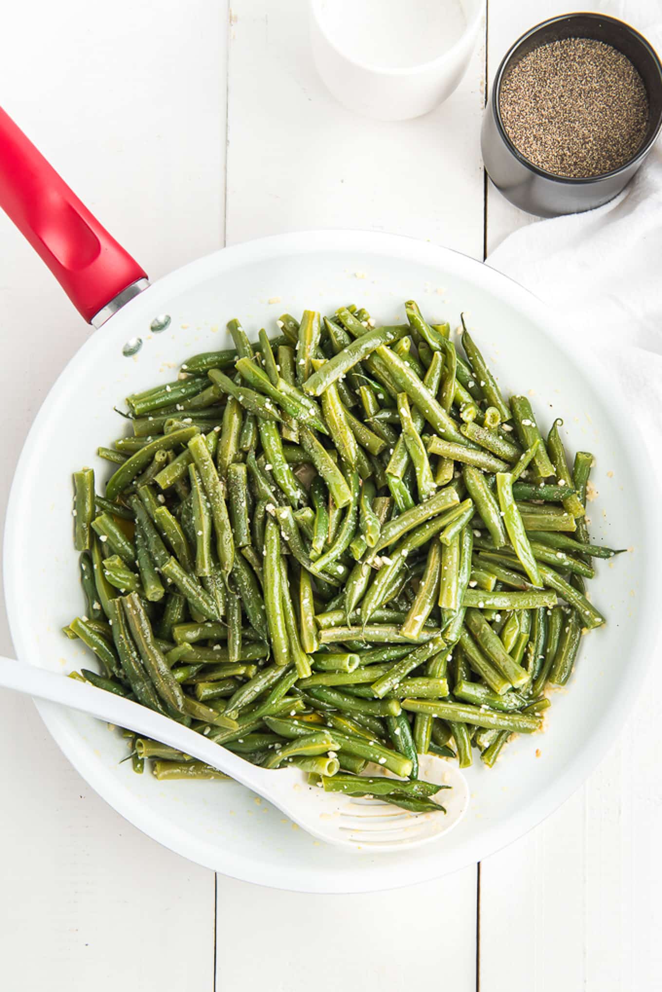 Blanched green beans in a skillet with a container of salt and pepper along with a white towel on the counter.