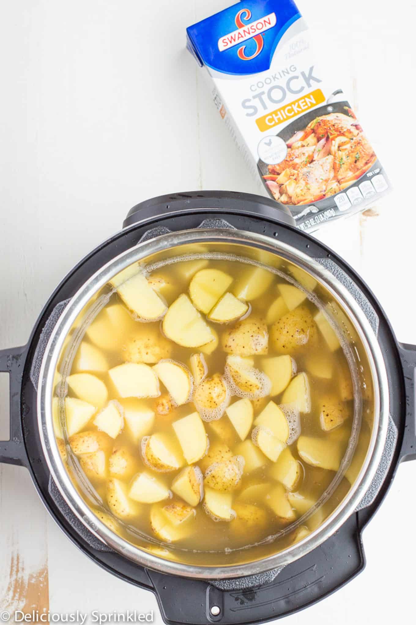 Cubes of potatoes in the instant pot with a container of broth to the side.