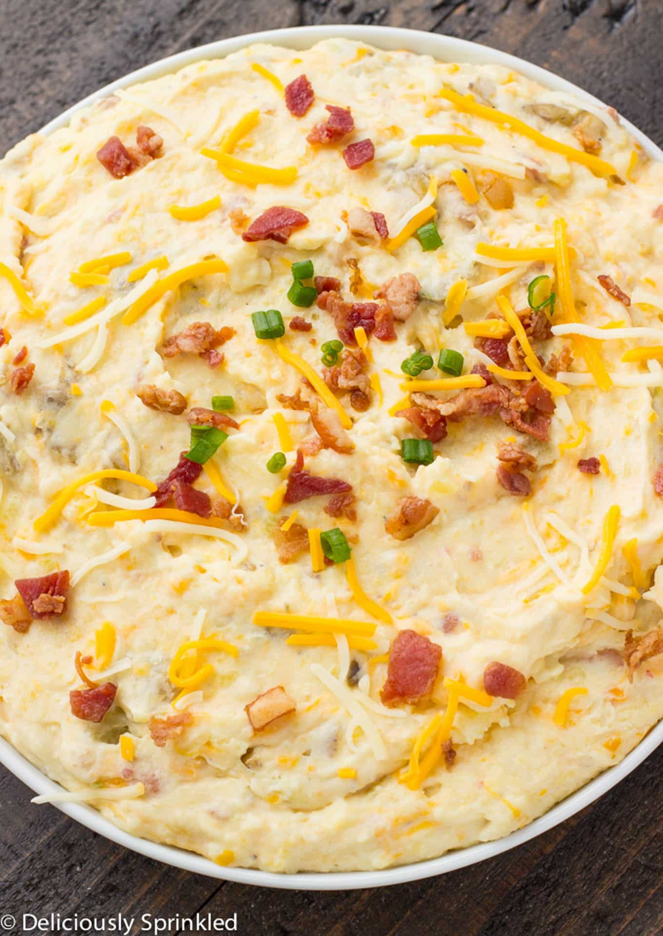Loaded mashed potatoes topped with some bacon, cheese, and green onions in a serving bowl on the table.