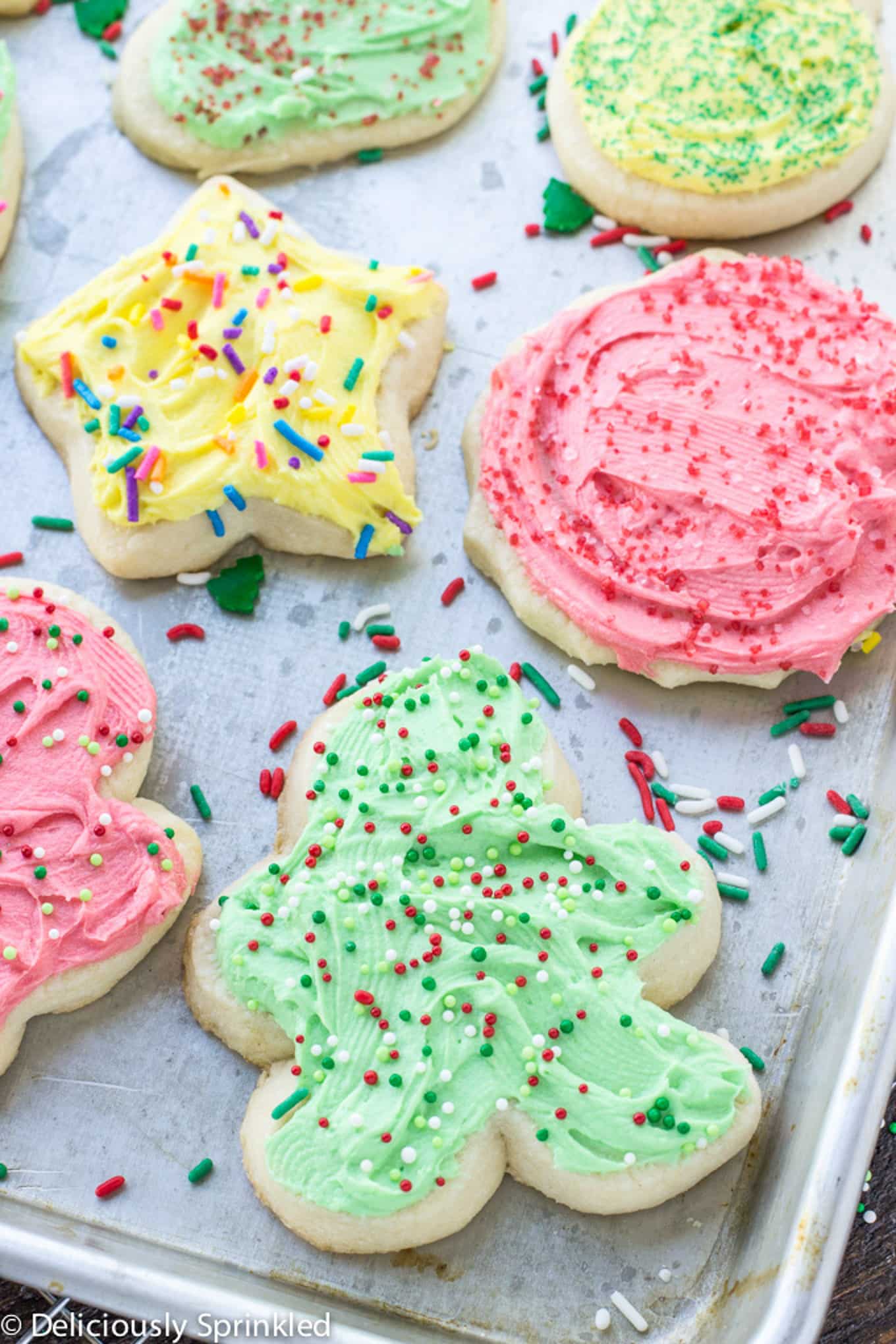 Traditional Christmas cookies on a baking pan topped with colored frosting and sprinkles.