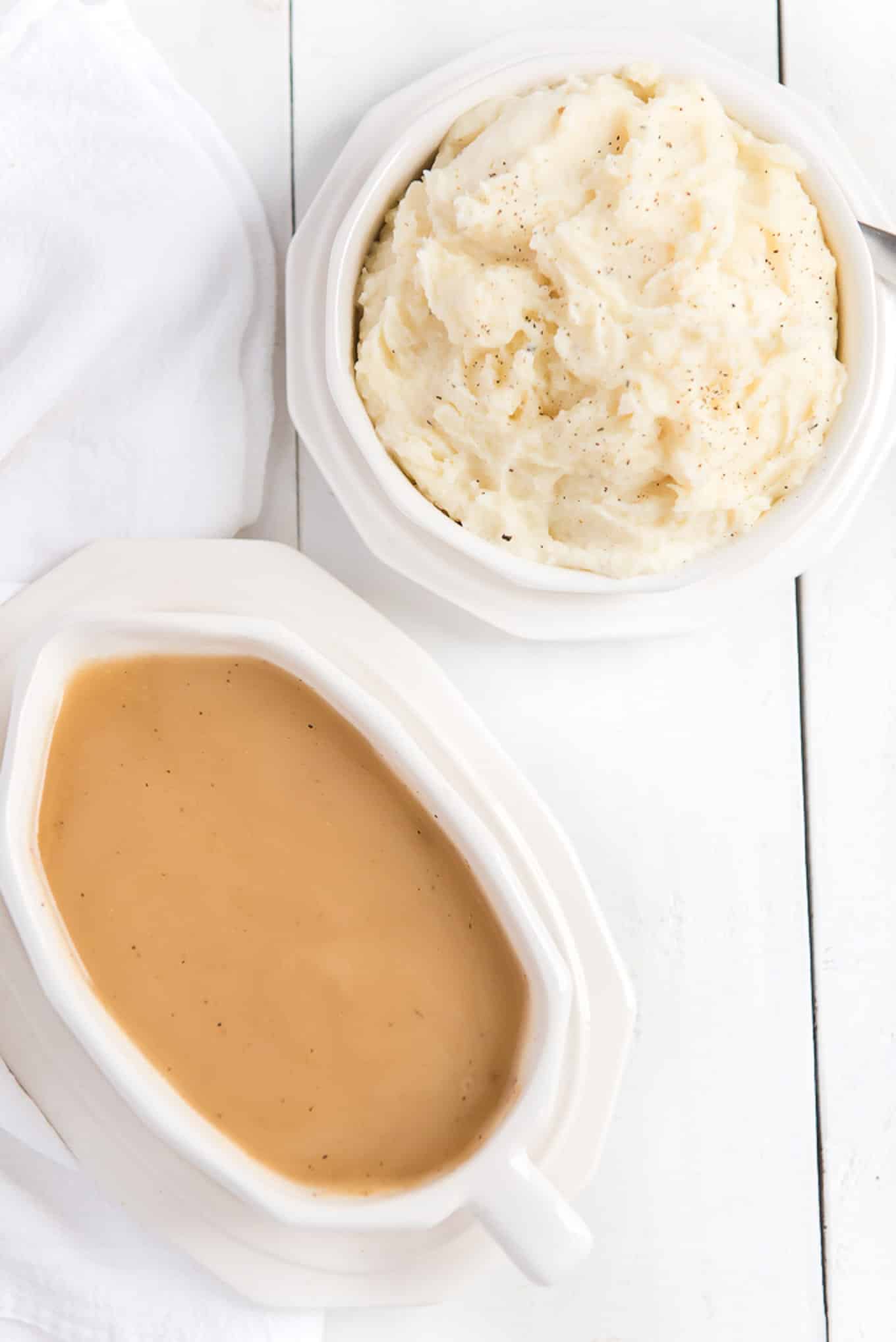 Gravy without drippings in a white serving dish on the table with a bowl of mashed potatoes next to it.
