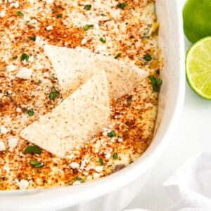 Street corn dip with tortilla chips and limes on the side.
