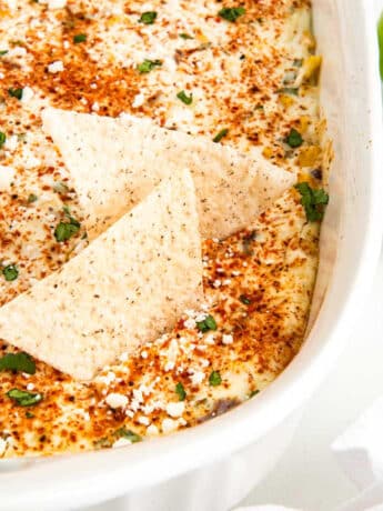 Street corn dip with tortilla chips and limes on the side.