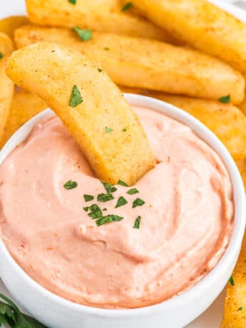 A bowl of fry sauce on a plate of fries with a french fry dipping in it.