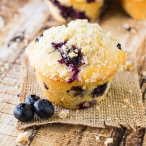 Homemade blueberry muffin on the table on a piece of burlap with blueberries to the side.
