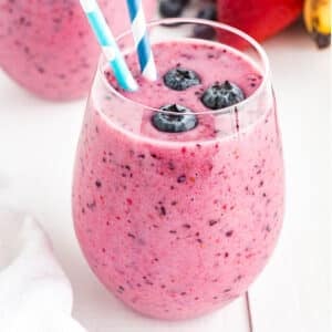 Glass of blueberry smoothie with blueberries and a straw.