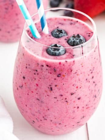 Glass of blueberry smoothie with blueberries and a straw.